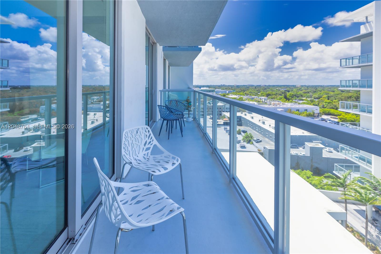 A balcony with white patterned chairs overlooks a city landscape under a blue sky — 3900 Biscayne Blvd # 1118, Miami FL 33137, MIAMI, FL