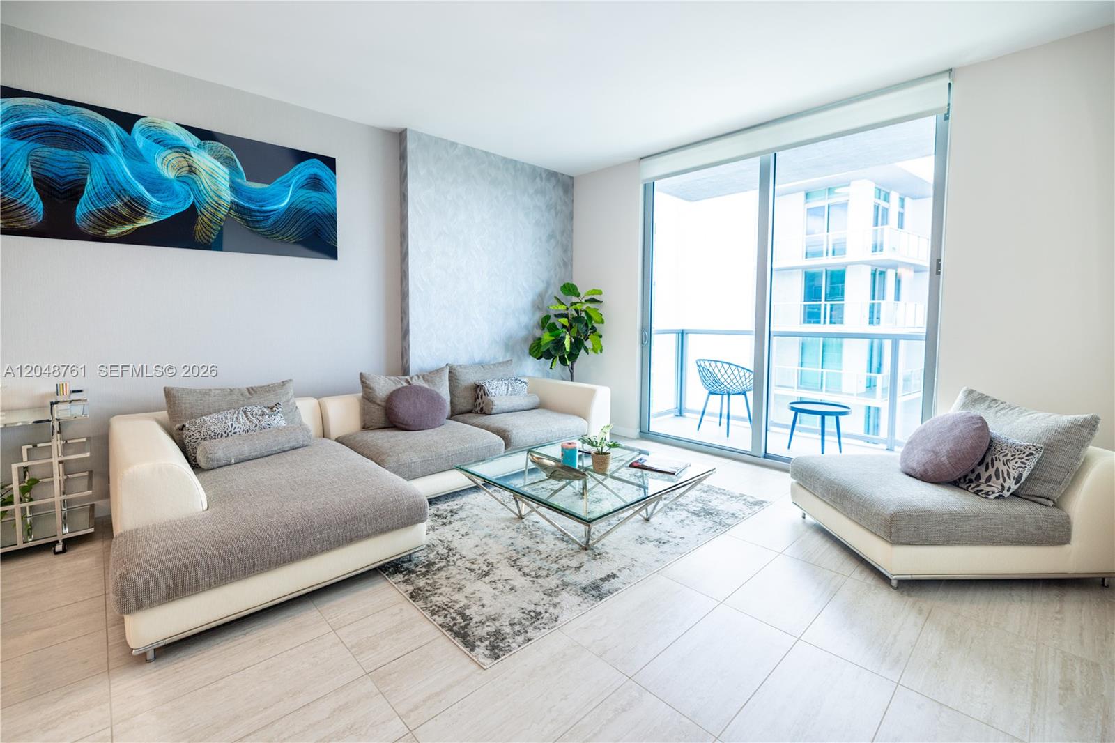 A modern living room features a large sectional sofa, glass coffee table, and balcony access — 3900 Biscayne Blvd # 1118, Miami FL 33137, MIAMI, FL
