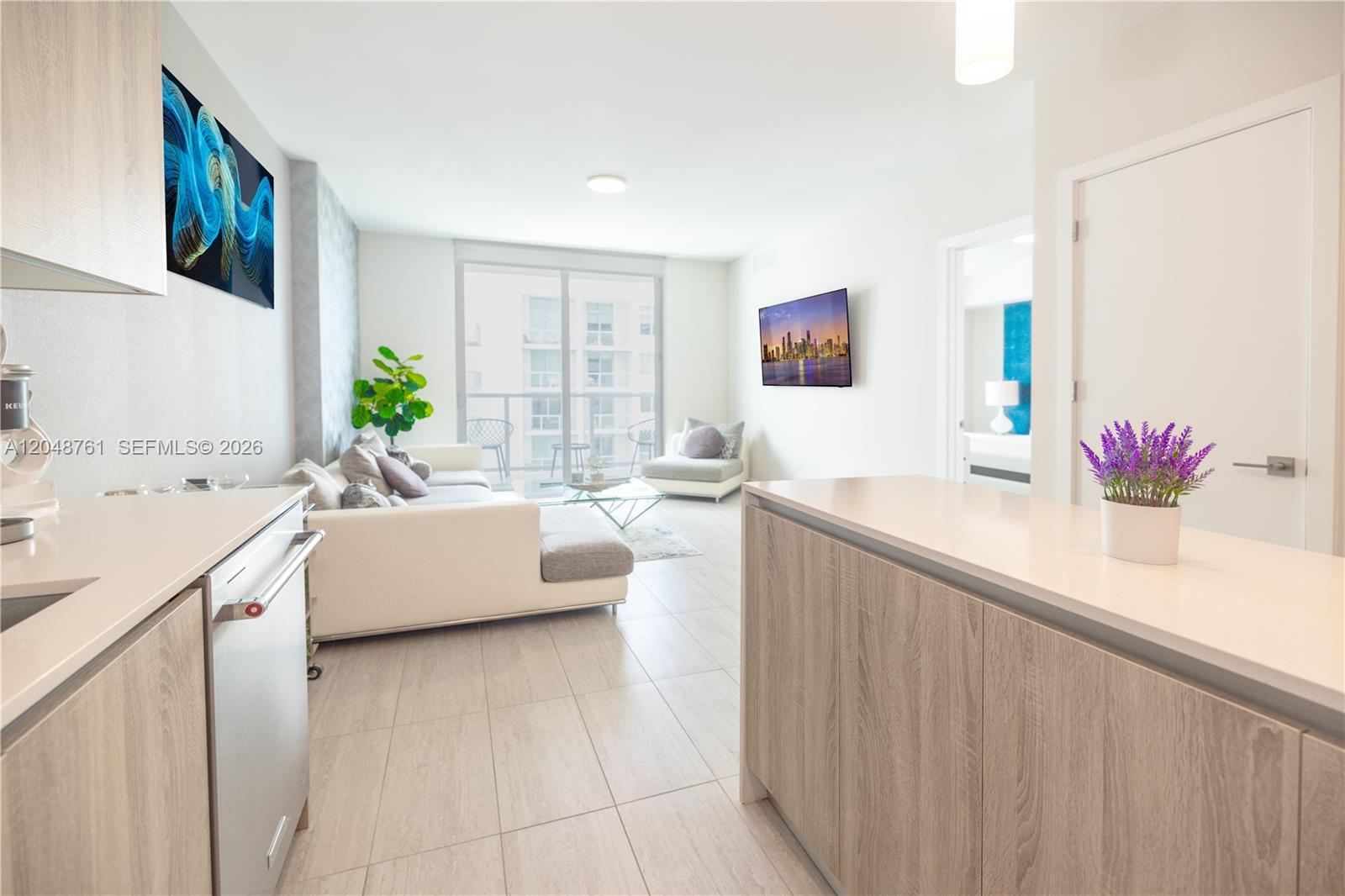 A modern apartment living area features a kitchen island, white sofa, and balcony access — 3900 Biscayne Blvd # 1118, Miami FL 33137, MIAMI, FL