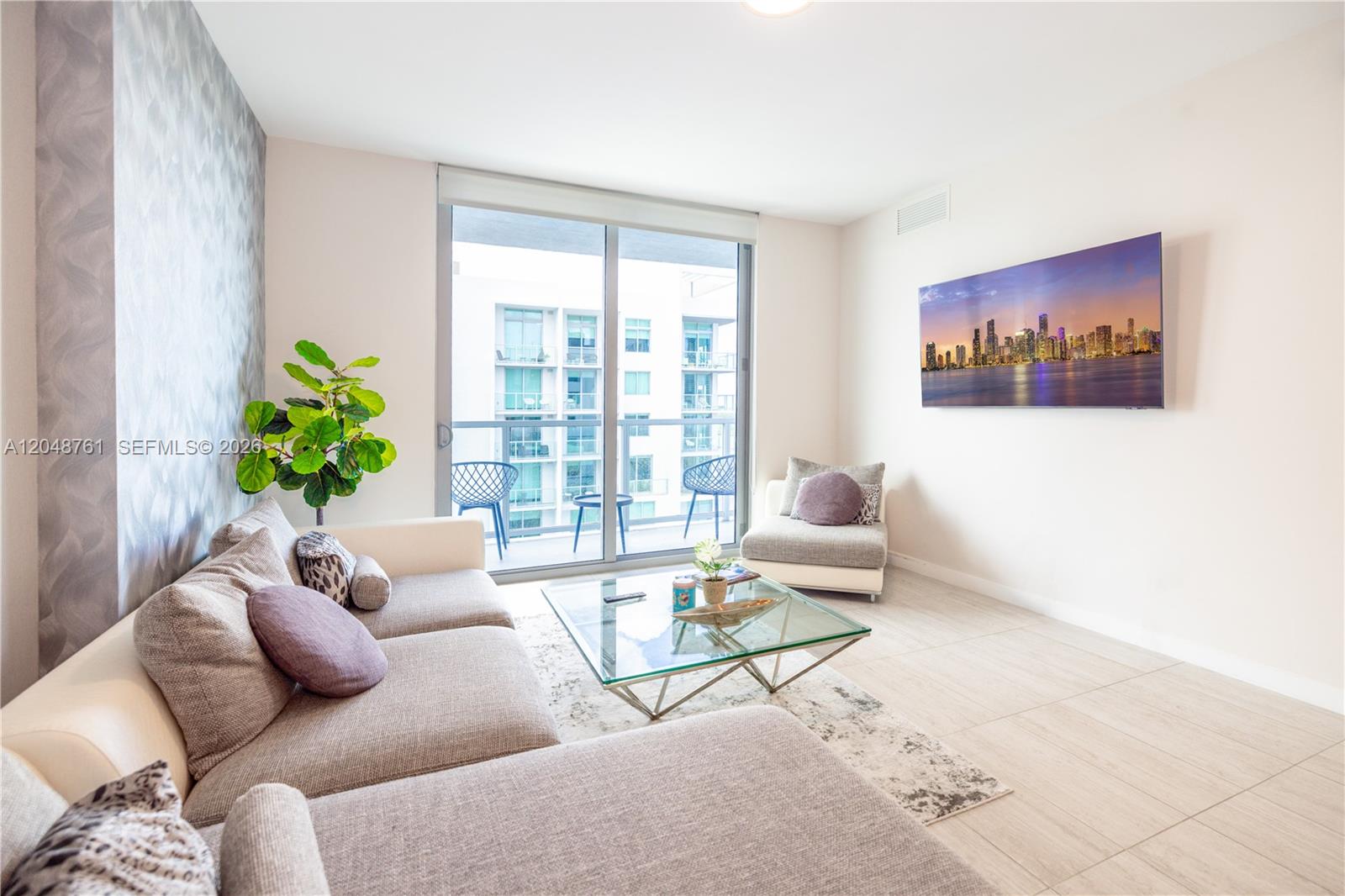 A living room features a sectional sofa, glass coffee table, and a wall-mounted television — 3900 Biscayne Blvd # 1118, Miami FL 33137, MIAMI, FL