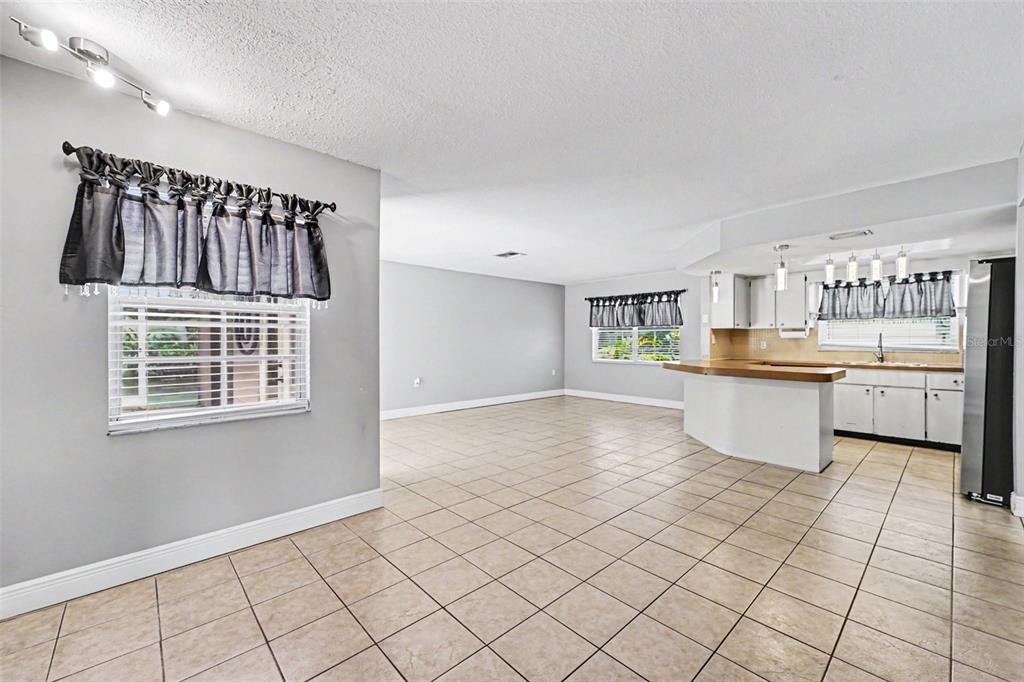An open-concept living and dining area features light gray walls, tile flooring, and a kitchen — 8040 SAYBROOK DRIVE, PORT RICHEY, FL