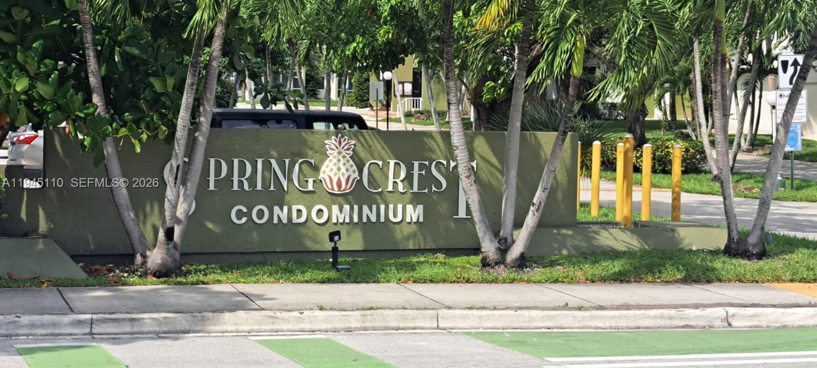 A green sign for Springcrest Condominium stands behind a sidewalk and palm trees — 4255 N University Dr # 315, Sunrise FL 33351, SUNRISE, FL
