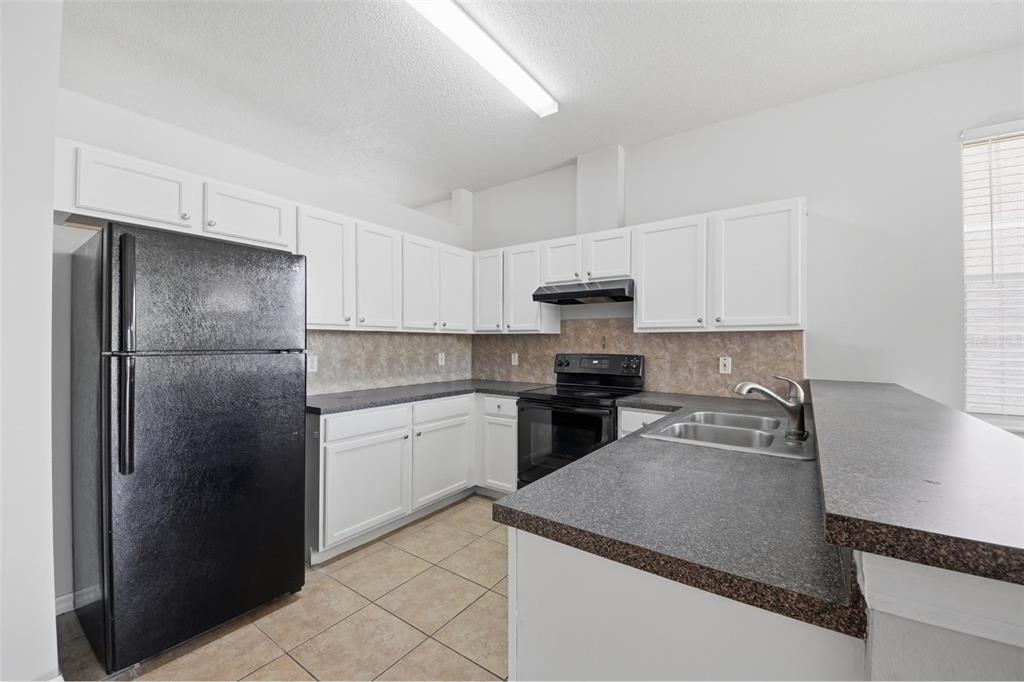 A kitchen features white cabinets, dark countertops, black appliances, and light-colored tile flooring — 949 WHISPERING CYPRESS LANE, ORLANDO, FL