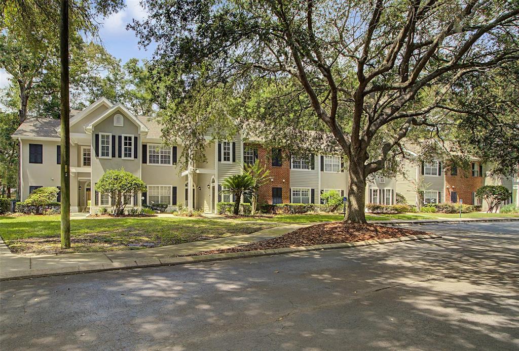 A multi-story apartment building with light siding and brick accents sits behind a large tree — 10000 SW 52ND AVENUE UNIT AA-159, GAINESVILLE, FL