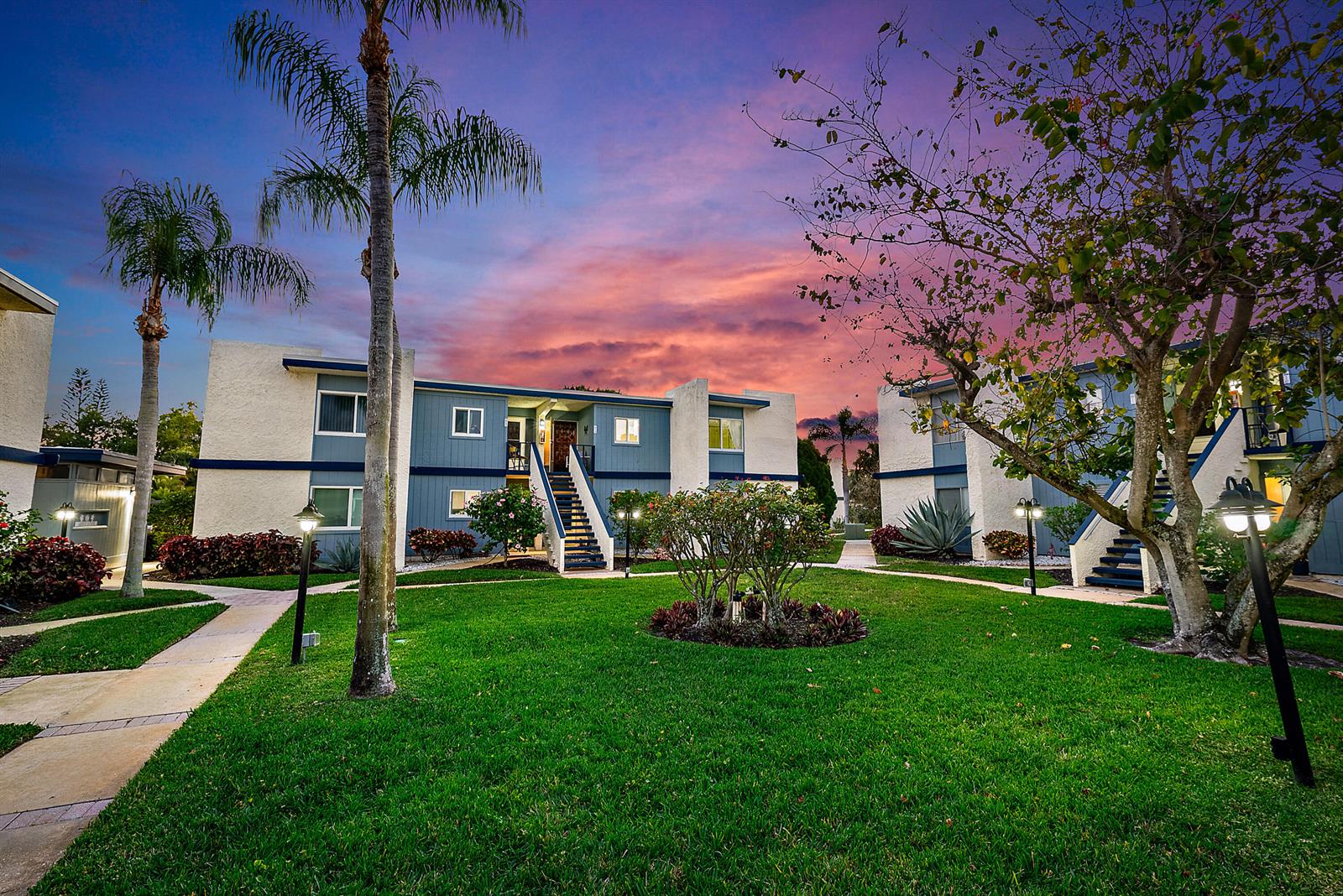 An exterior view of a two-story apartment complex with a grassy courtyard at sunset — 1561 NE 12th Terrace # C14, Jensen Beach FL 34957, JENSEN BEACH, FL