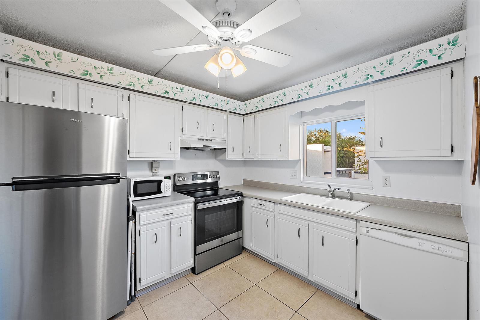 A kitchen with white cabinets, stainless steel appliances, tile flooring, and a ceiling fan — 1561 NE 12th Terrace # C14, Jensen Beach FL 34957, JENSEN BEACH, FL