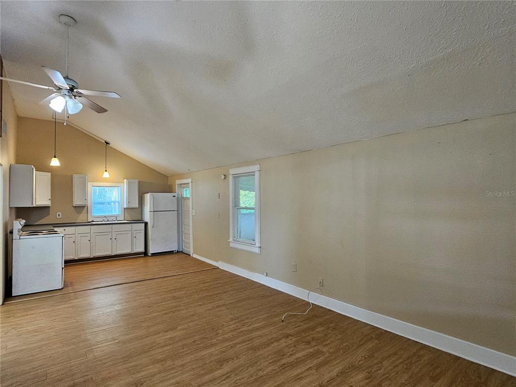 An open-concept kitchen and living area features vaulted ceilings, wood-look flooring, and white cabinetry — 2441 E MAGNOLIA STREET, LAKELAND, FL
