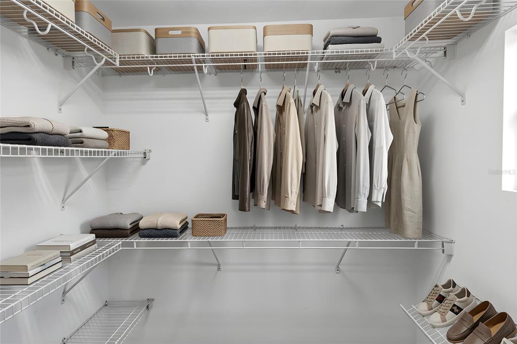 A walk-in closet features white wire shelving, hanging clothes, folded garments, and a few pairs of shoes — 4849 NW 46TH AVENUE, OCALA, FL