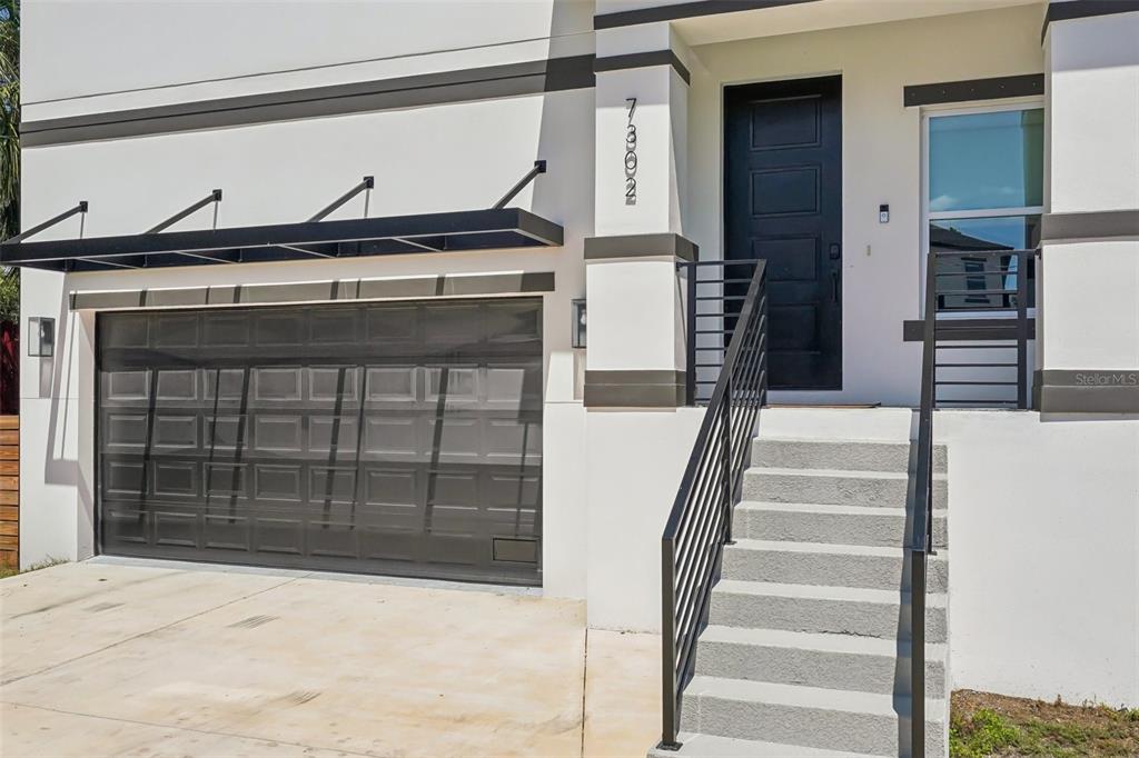 A modern home exterior features a garage, a front door, and concrete stairs with railings — 7302 S ELLIOTT STREET, TAMPA, FL