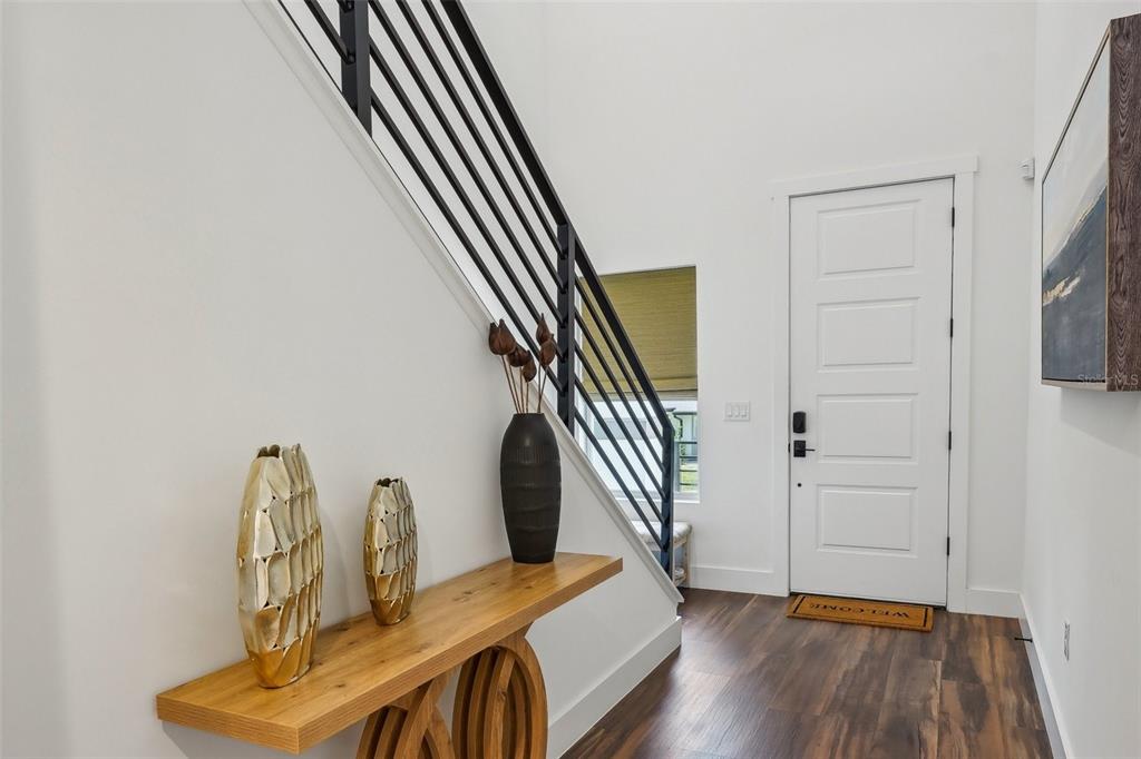 A modern entryway features a wooden console table, a black staircase railing, and white walls — 7302 S ELLIOTT STREET, TAMPA, FL