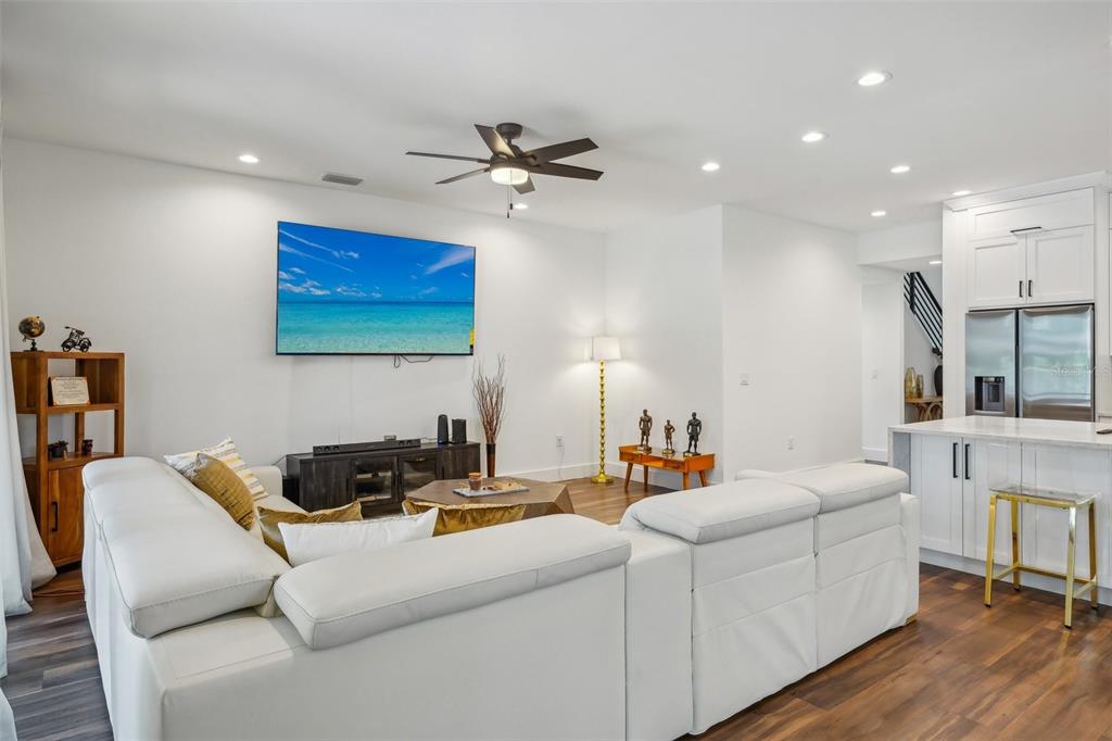 A living room features a white sectional sofa, a wall-mounted television, and a kitchen area — 7302 S ELLIOTT STREET, TAMPA, FL