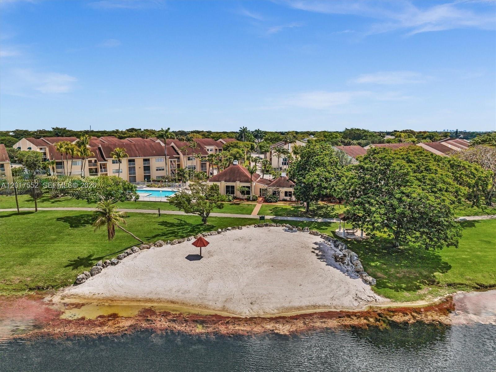 An aerial view shows a sandy beach area with a red umbrella beside a lake — 15320 SW 106th Ter # 1108, Miami FL 33196, MIAMI, FL