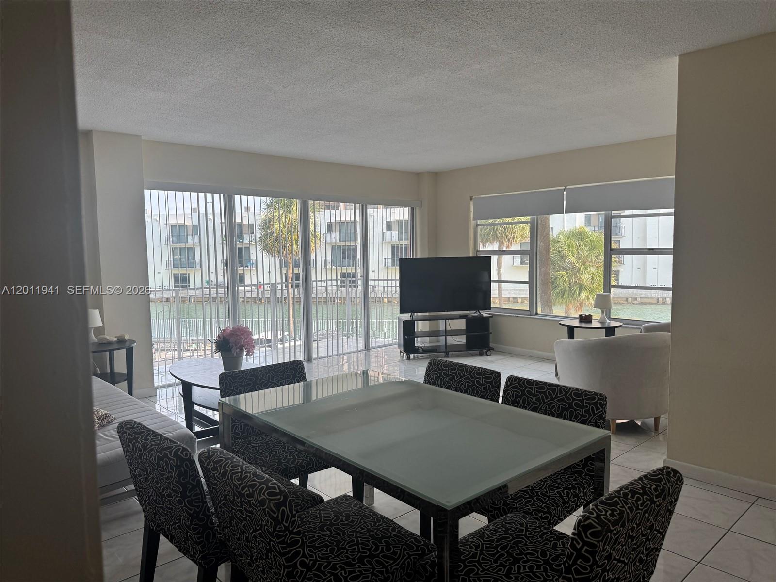 A dining area and living room with tile floors overlook a canal through large windows — 11111 Biscayne Blvd # 2H, Miami FL 33181, MIAMI, FL