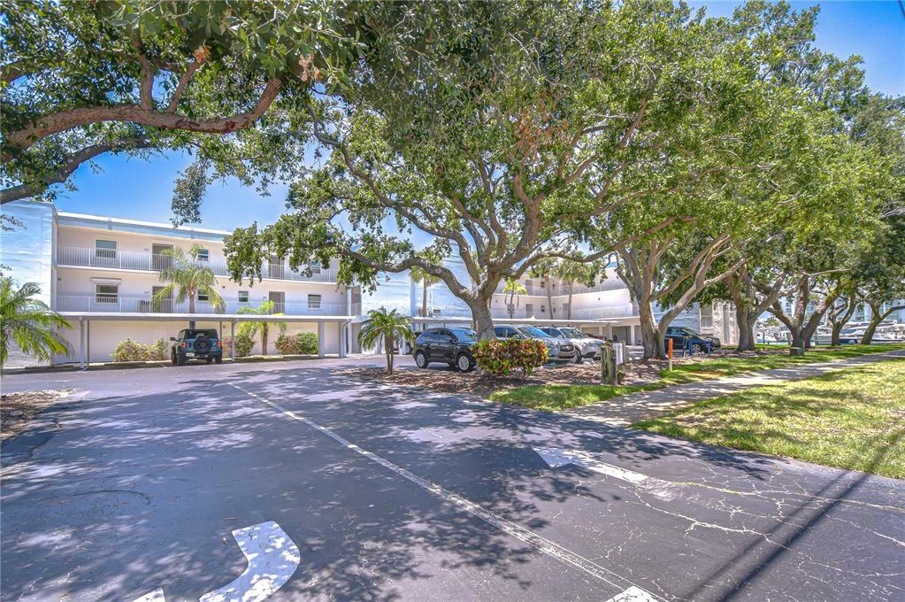 A multi-story apartment building with covered parking spaces sits beneath large, mature shade trees — 340 PINELLAS BAYWAY S UNIT 304, ST PETERSBURG, FL