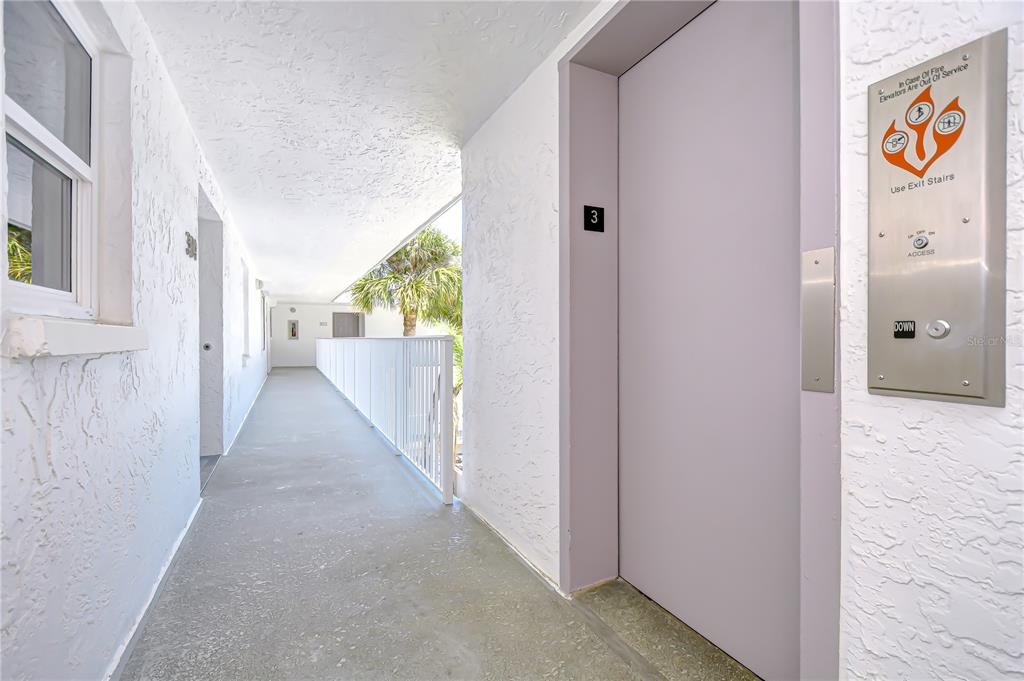 An outdoor apartment hallway features a gray elevator door and a white metal railing — 340 PINELLAS BAYWAY S UNIT 304, ST PETERSBURG, FL