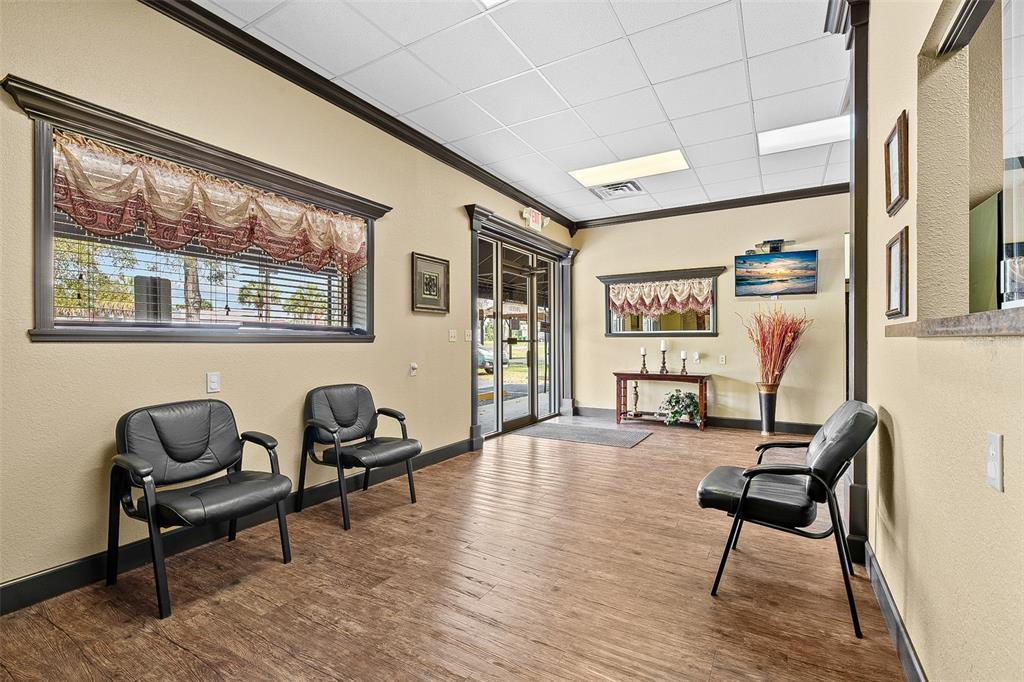 A waiting room features wood-look flooring, black chairs, a window with valances, and a doorway — 1411 NW 23RD AVENUE, CHIEFLAND, FL
