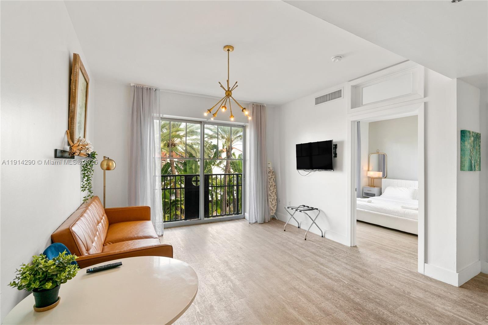 A living room with a leather sofa, light wood flooring, and a view of palm trees — 1060 Ocean Dr # D307, Miami Beach FL 33139, MIAMI BEACH, FL