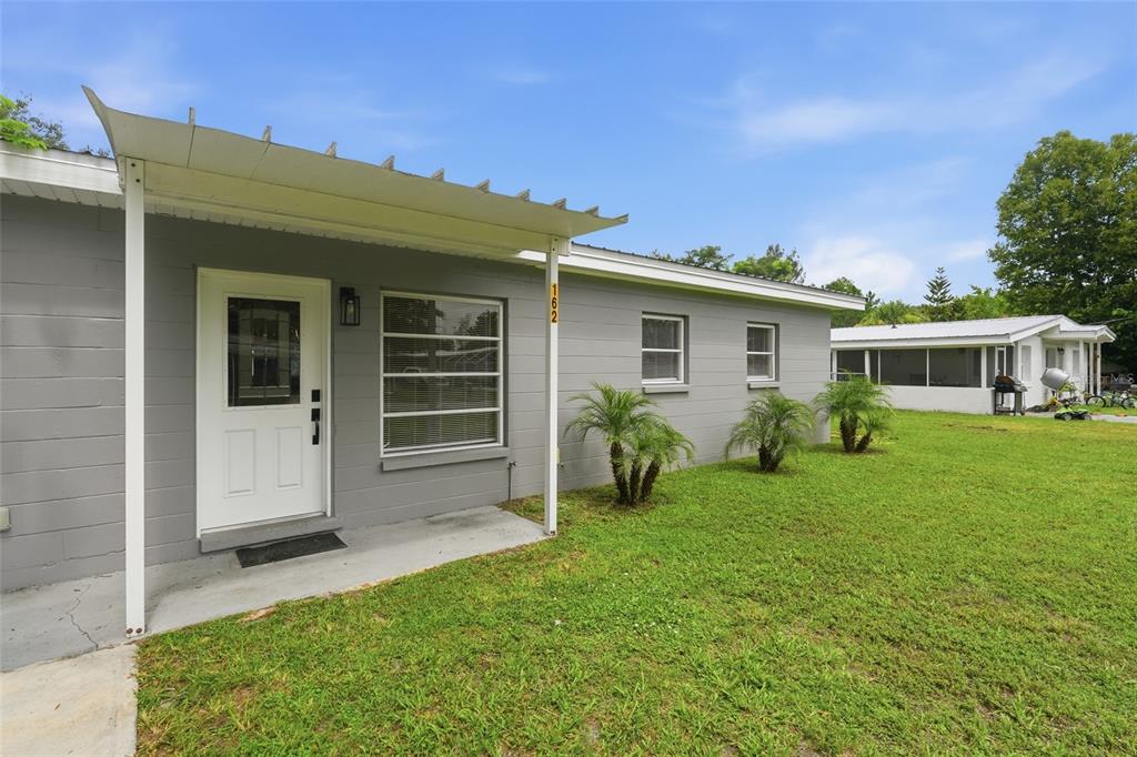 A gray concrete block house with a white door, metal awning, and a grassy yard — 162 BRIDLE PATH, ARCADIA, FL
