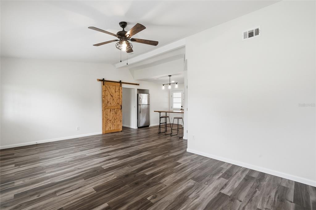 An open-concept room features wood-look flooring, a ceiling fan, and a sliding barn door — 162 BRIDLE PATH, ARCADIA, FL