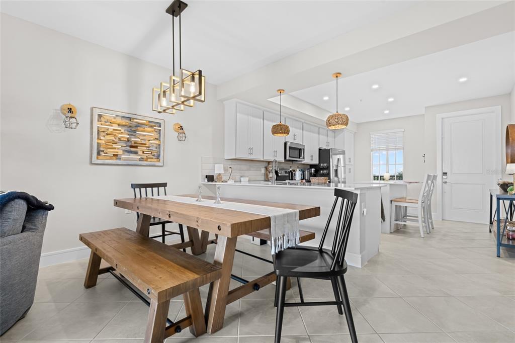 A dining area with a wooden table and bench sits in front of an open kitchen — 5651 DOUBLE EAGLE CIRCLE UNIT 4335, AVE MARIA, FL