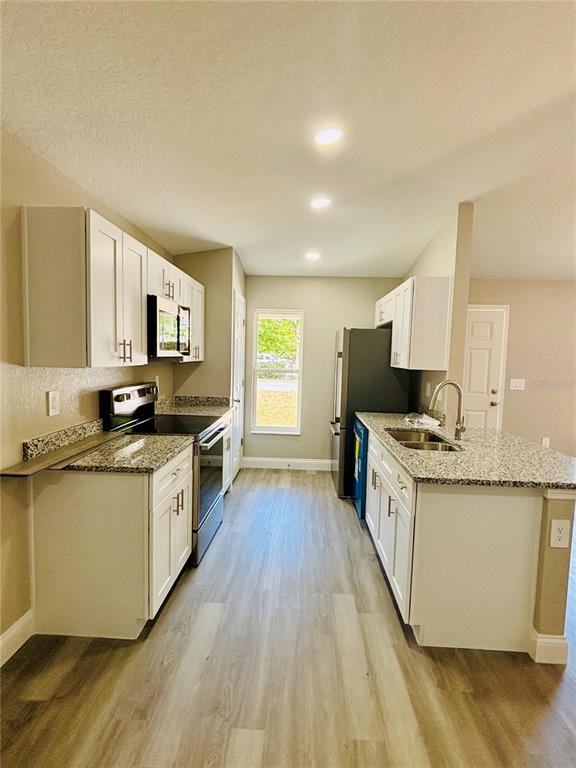 A kitchen features white cabinets, granite countertops, stainless steel appliances, and light wood-look flooring — 25 PALMETTO AVENUE S, FORT MEADE, FL