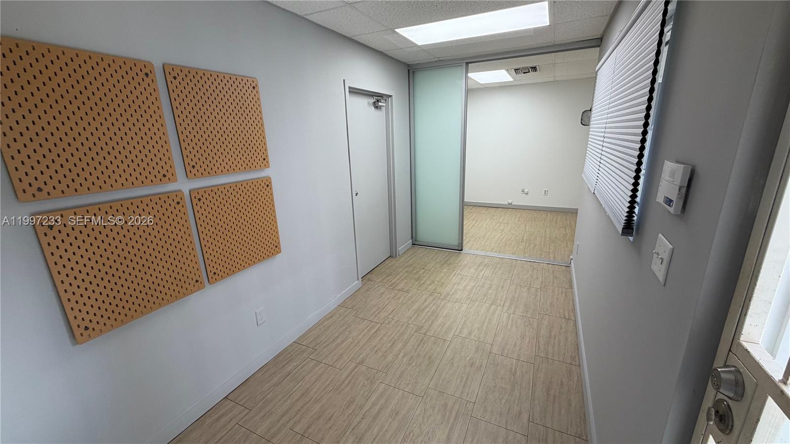An office hallway features wood-look flooring, four pegboards on the wall, and a sliding glass door — 10859 NW 29th St # 10859, Doral FL 33172, DORAL, FL