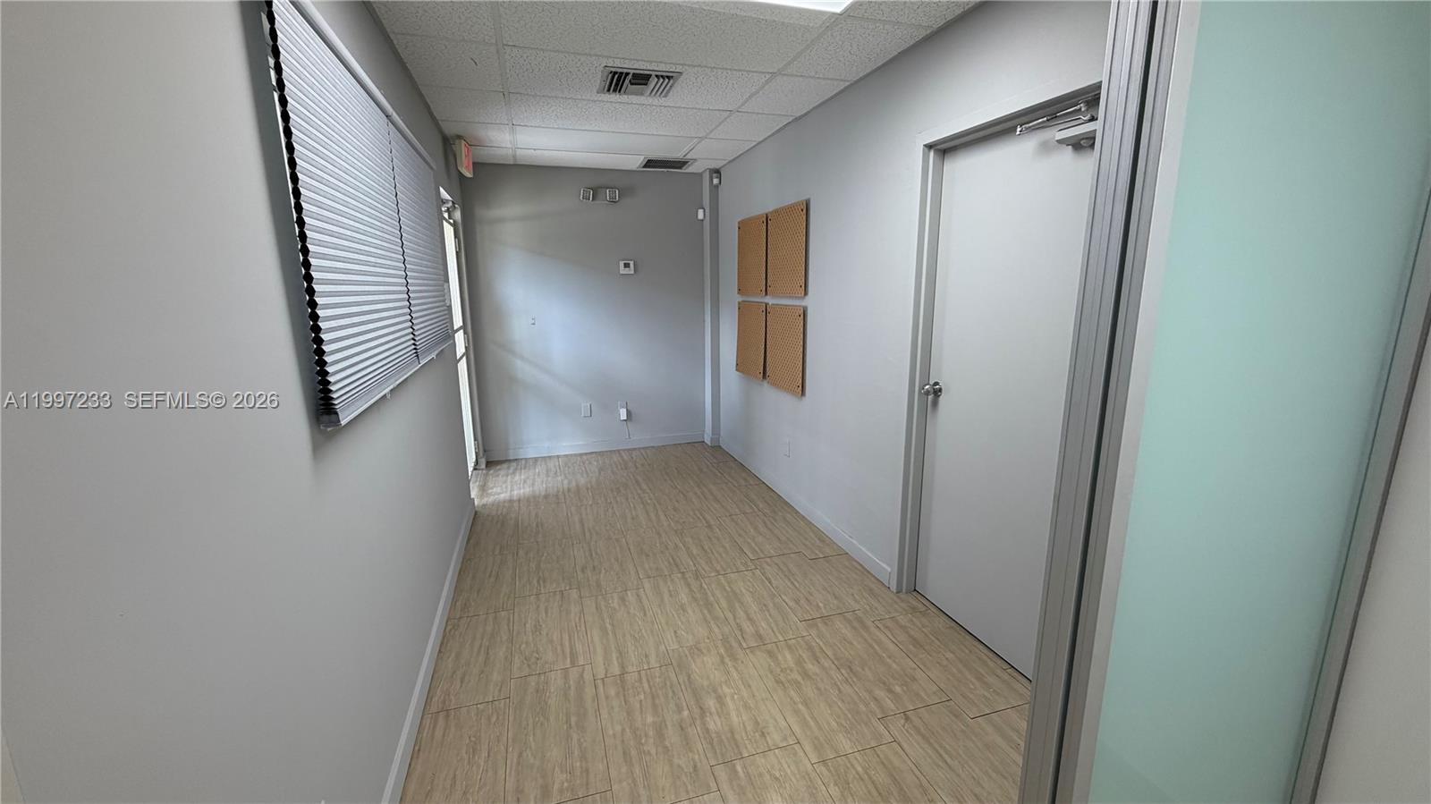 A narrow office hallway features light wood-look tile flooring, gray walls, and a closed door — 10859 NW 29th St # 10859, Doral FL 33172, DORAL, FL