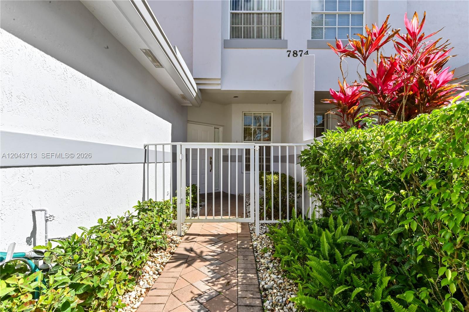A white metal gate leads to a paved walkway and entrance of a residential building — 7874 Laina Ln # 1, Boynton Beach FL 33437, BOYNTON BEACH, FL