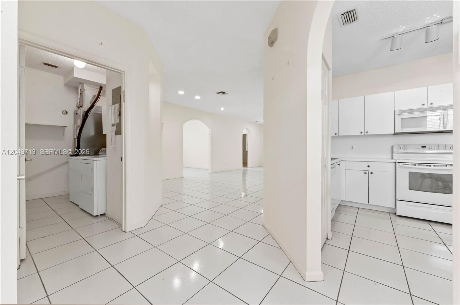 A white-tiled interior view showing a laundry room, a kitchen, and an open living area — 7874 Laina Ln # 1, Boynton Beach FL 33437, BOYNTON BEACH, FL