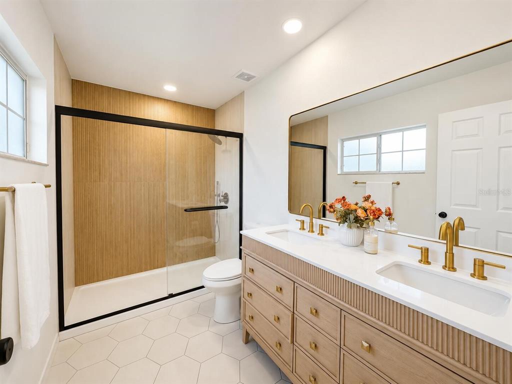 A modern bathroom features a wood-paneled shower, double vanity with gold fixtures, and hexagonal flooring — 11348 NW 31ST LANE, GAINESVILLE, FL
