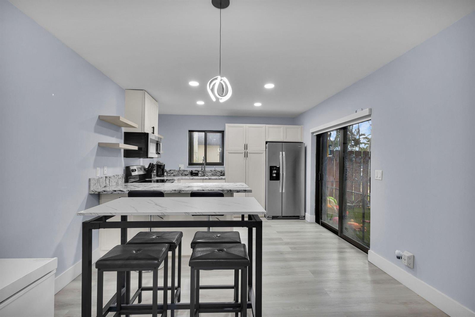 A kitchen features white cabinets, marble-look countertops, a stainless steel refrigerator, and a dining table — 2824 Kirk Road, Lake Worth FL 33461, LAKE WORTH, FL