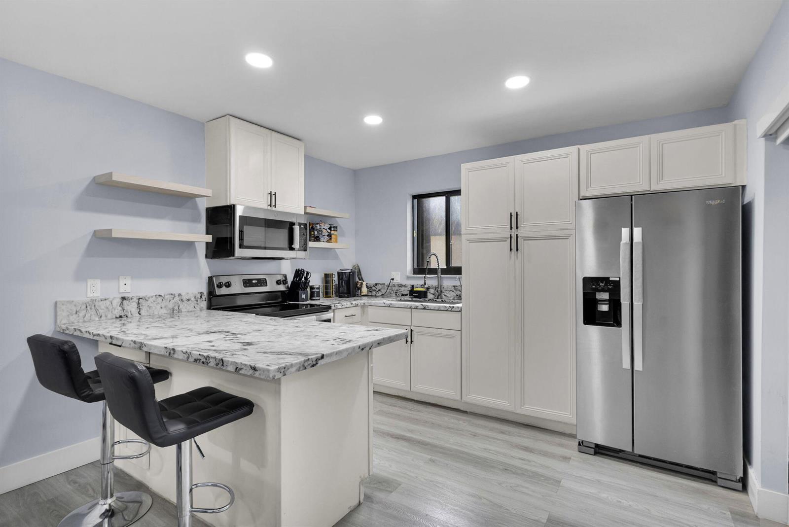 A kitchen features white cabinets, marble-patterned countertops, stainless steel appliances, and two black bar stools — 2824 Kirk Road, Lake Worth FL 33461, LAKE WORTH, FL