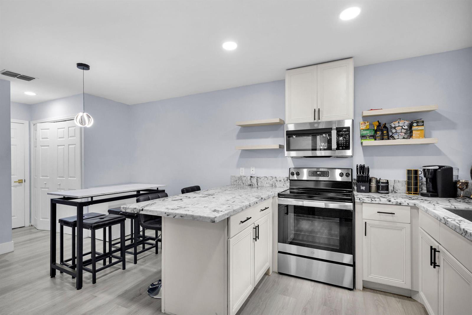 A kitchen features white cabinets, granite countertops, stainless steel appliances, and a breakfast bar area — 2824 Kirk Road, Lake Worth FL 33461, LAKE WORTH, FL