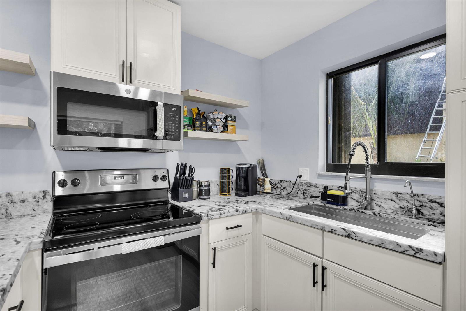 A kitchen features white cabinets, marble-patterned countertops, stainless steel appliances, and a window view — 2824 Kirk Road, Lake Worth FL 33461, LAKE WORTH, FL