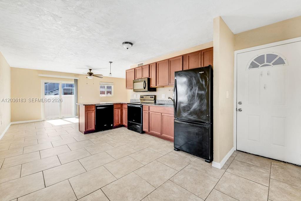 A kitchen with wood cabinets and black appliances opens into a living area with tile — 2550 Tulane Ave # 101, Daytona FL 32118, DAYTONA, FL