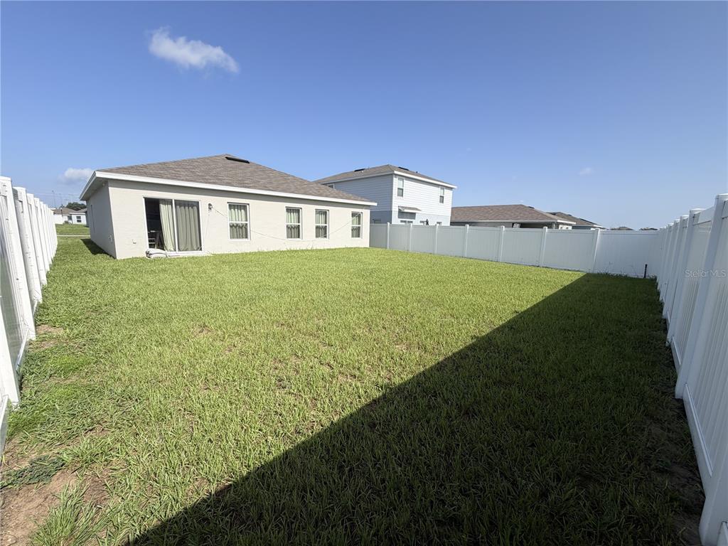 A fenced-in backyard features a grassy lawn behind a single-story house with sliding doors — 1427 MADISON CIRCLE, HAINES CITY, FL