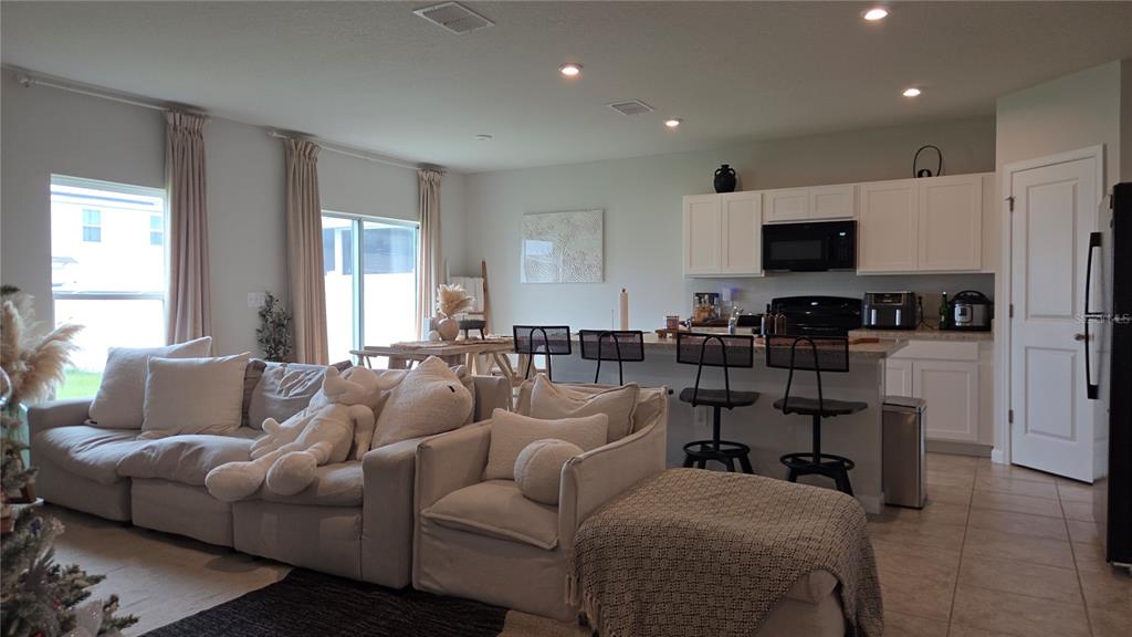 This open-concept living room and kitchen features white cabinetry, a breakfast bar, and neutral furniture — 1427 MADISON CIRCLE, HAINES CITY, FL