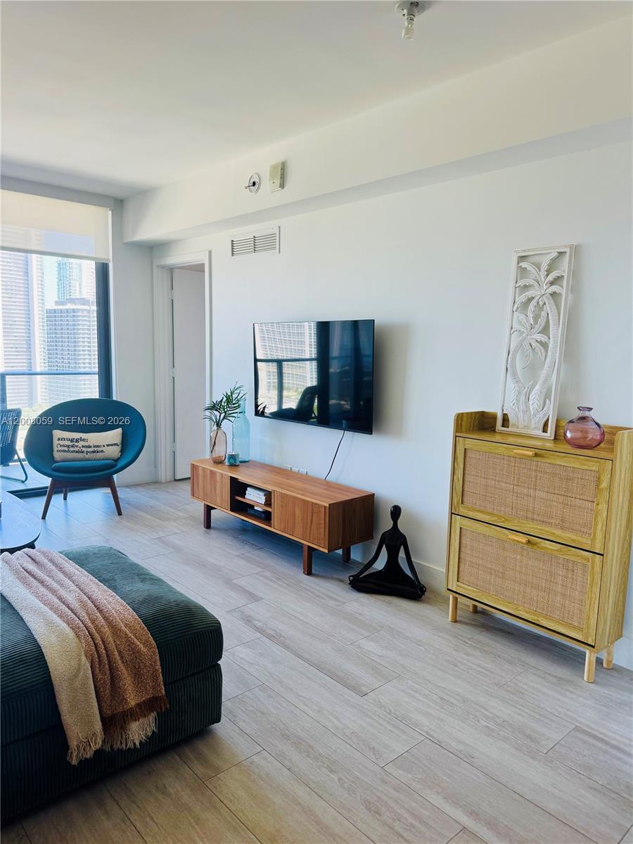 A modern living room features a wall-mounted television, wooden media console, and a rattan cabinet — 121 NE 34th St # 2705, Miami FL 33137, MIAMI, FL