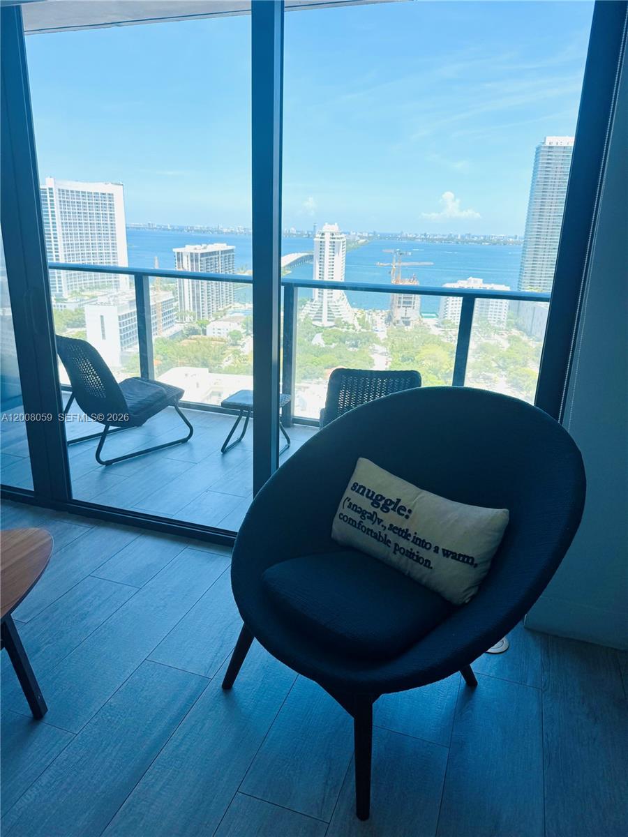 A modern room features a dark armchair with a decorative pillow facing a balcony view — 121 NE 34th St # 2705, Miami FL 33137, MIAMI, FL