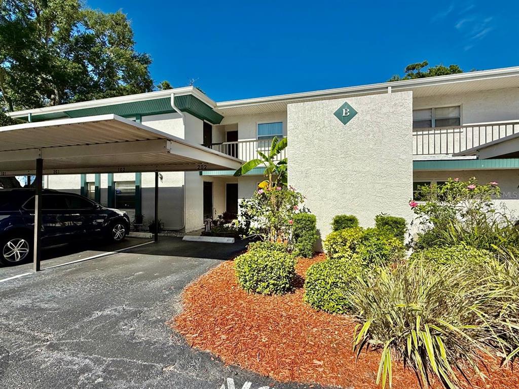 A two-story apartment building exterior features a covered parking area and landscaped mulch beds — 7560 92ND STREET UNIT 102B, SEMINOLE, FL