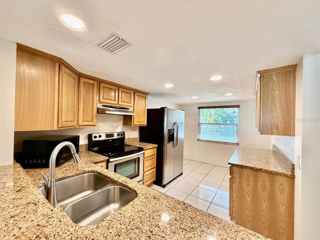 A kitchen features light wood cabinets, granite countertops, stainless steel appliances, and tile flooring — 7560 92ND STREET UNIT 102B, SEMINOLE, FL