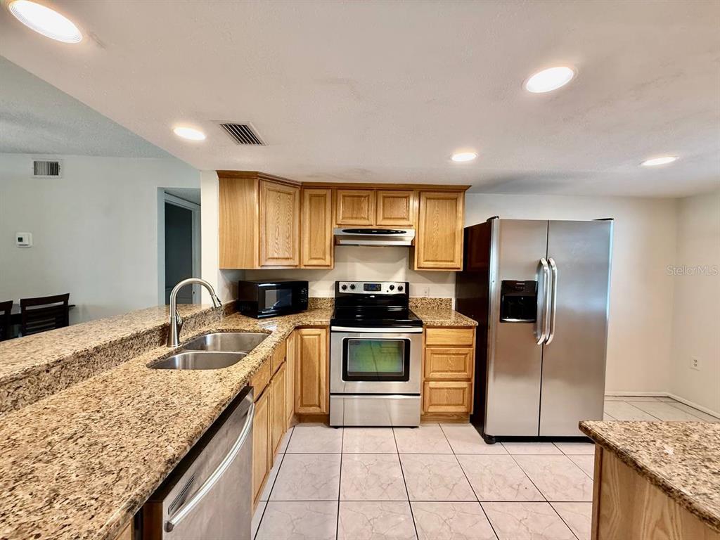A kitchen with light wood cabinets, granite countertops, and stainless steel appliances — 7560 92ND STREET UNIT 102B, SEMINOLE, FL