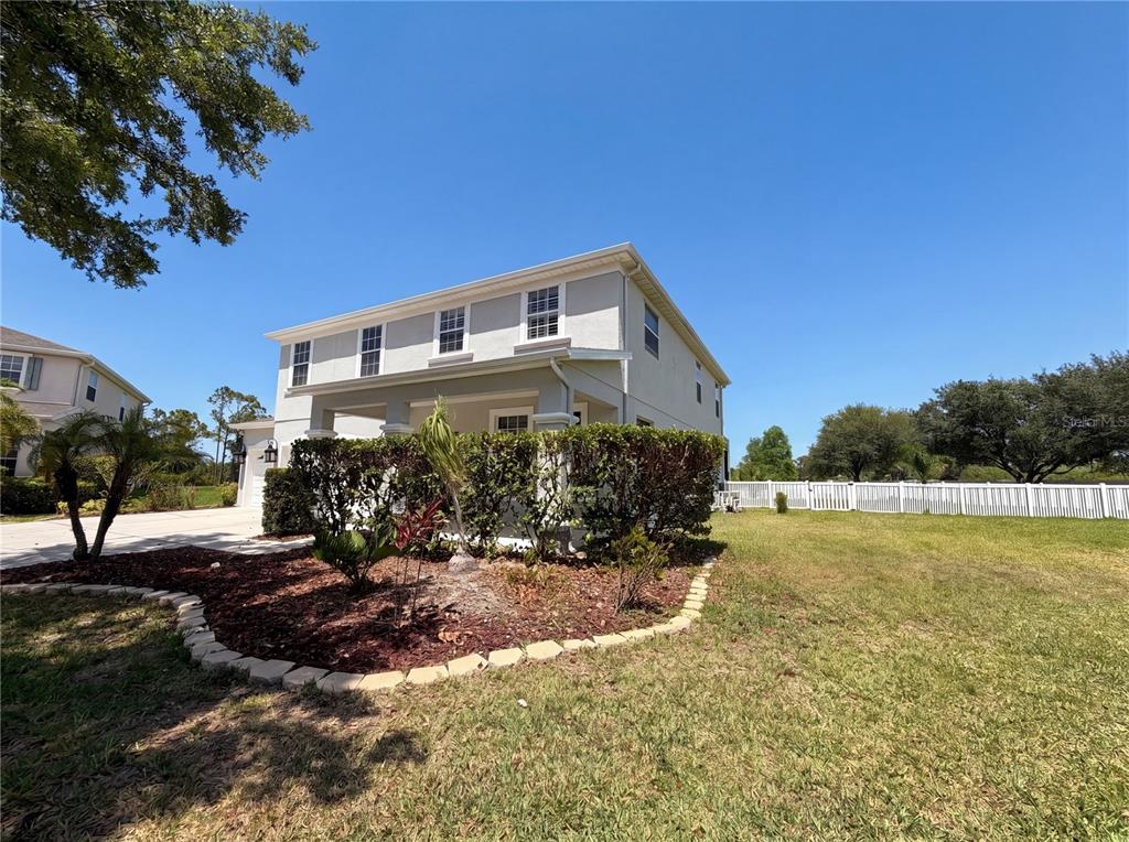 A two-story house with a covered front porch, landscaping, and a white vinyl fence — 1714 BOTTLEBRUSH WAY, NORTH PORT, FL