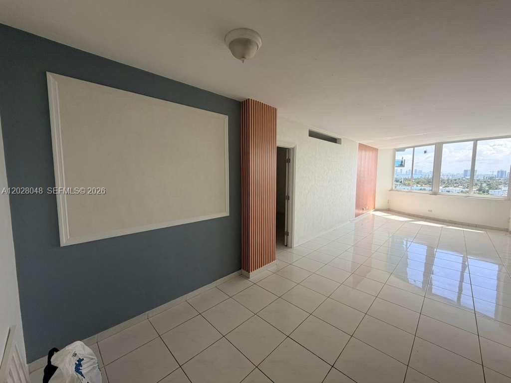 A bright, tiled living room features a blue accent wall with molding and floor-to-ceiling windows — 7441 Wayne Ave # 14D, Miami Beach FL 33141, MIAMI BEACH, FL
