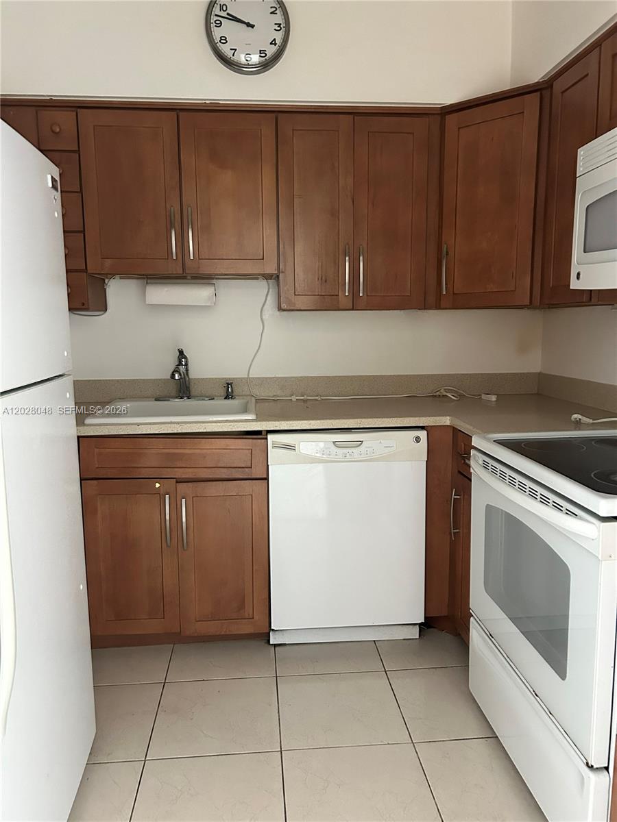 A kitchen features wood cabinets, white appliances, a sink, and light-colored tile flooring — 7441 Wayne Ave # 14D, Miami Beach FL 33141, MIAMI BEACH, FL