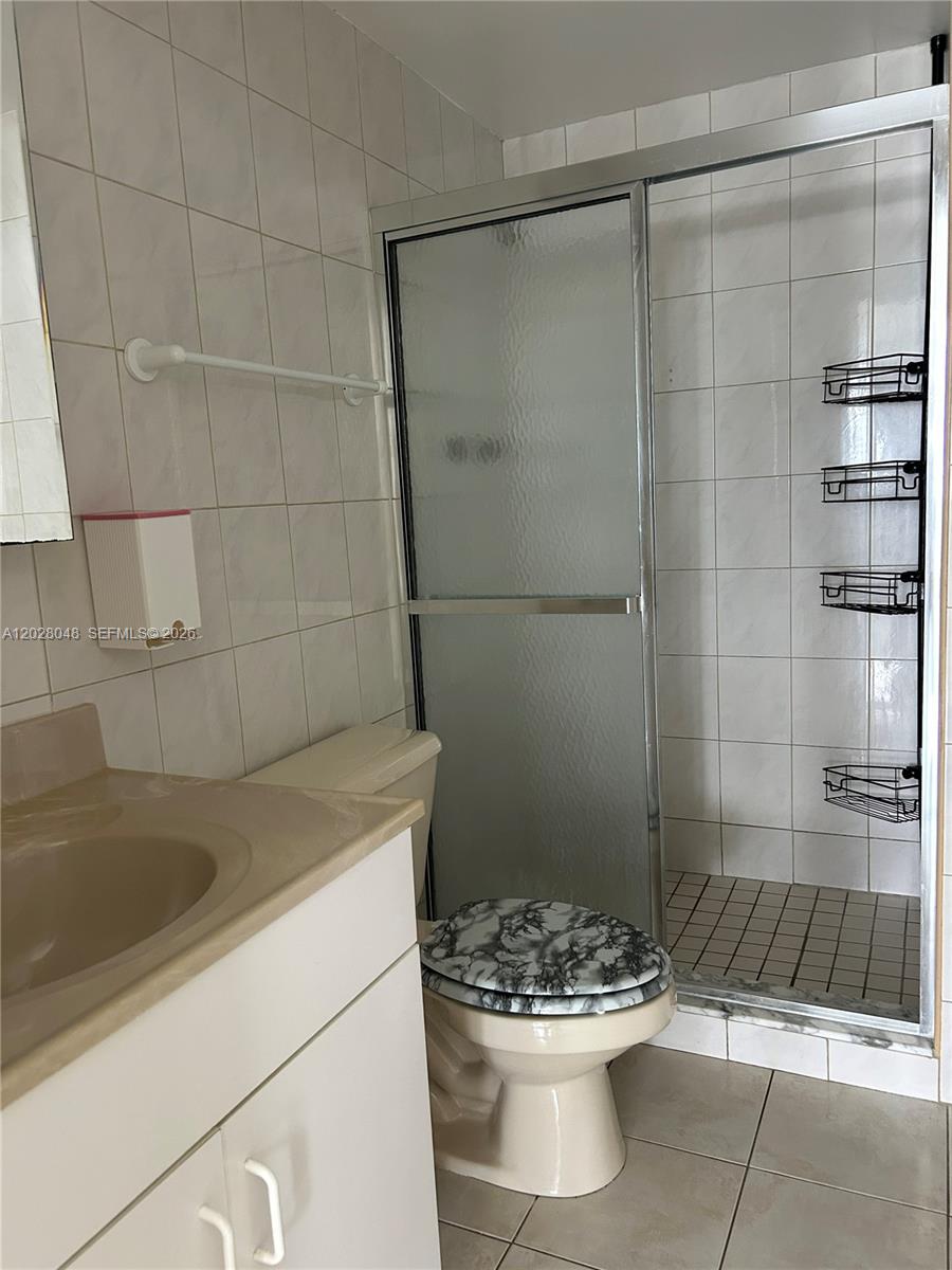 A bathroom features a vanity, a toilet with a patterned seat, and a glass-enclosed shower — 7441 Wayne Ave # 14D, Miami Beach FL 33141, MIAMI BEACH, FL