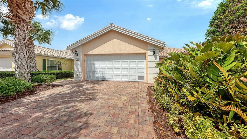 A paved driveway leads to a single-story house with a white garage door and landscaping — 11605 GARESSIO LANE, SARASOTA, FL