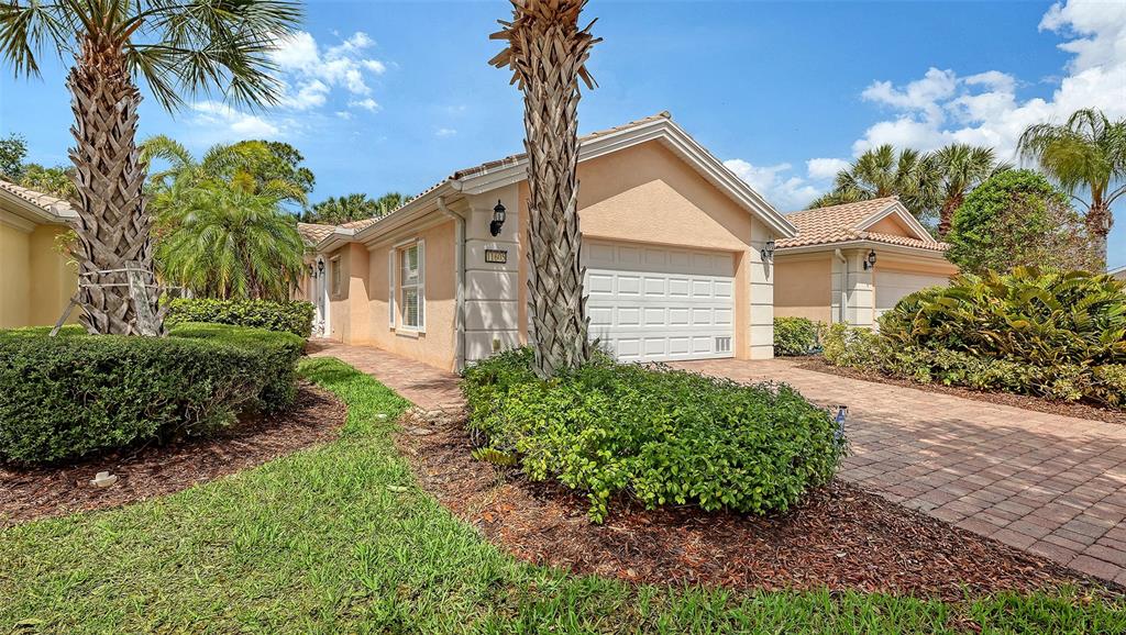 A single-story house with a beige stucco exterior, a white garage door, and palm trees — 11605 GARESSIO LANE, SARASOTA, FL