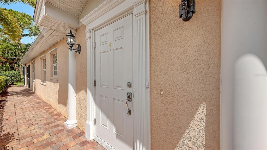 A white front door with a handle set is set into a beige stucco exterior wall — 11605 GARESSIO LANE, SARASOTA, FL