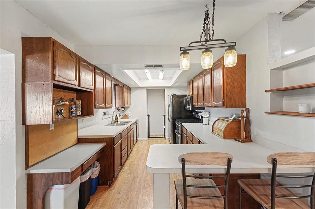 A galley-style kitchen features wood cabinets, white countertops, a breakfast bar, and pendant lighting — 5967 102ND AVENUE N, PINELLAS PARK, FL